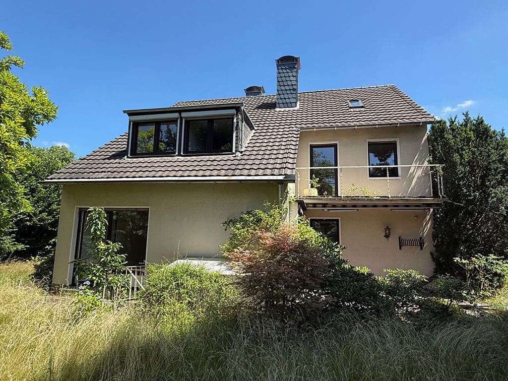 Rückansicht vor der Kernsanierung. Rückansicht eines Wohngebäudes in Köln-Rath vor der Kernsanierung mit bestehender Dachgaube, Dachflächenfenster und Gartenansicht.