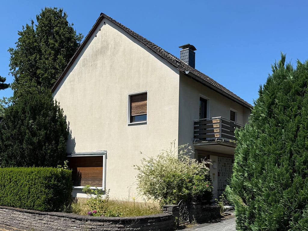 Vorderansicht vor der Kernsanierung. Vorderansicht eines Wohngebäudes in Köln-Rath vor der Kernsanierung mit Balkon, Eingangsbereich und bestehender Fassadengestaltung.
